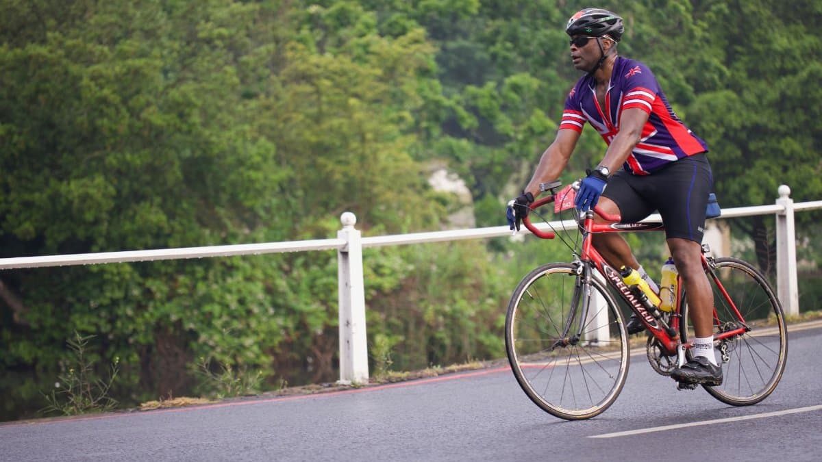 A cyclist in vibrant gear rides a red road bike along a scenic forest road.