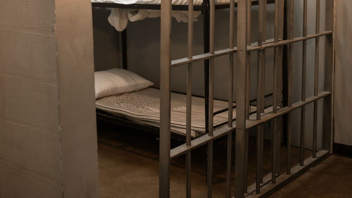 A prison cell featuring a metal bunk bed and striped sheets.