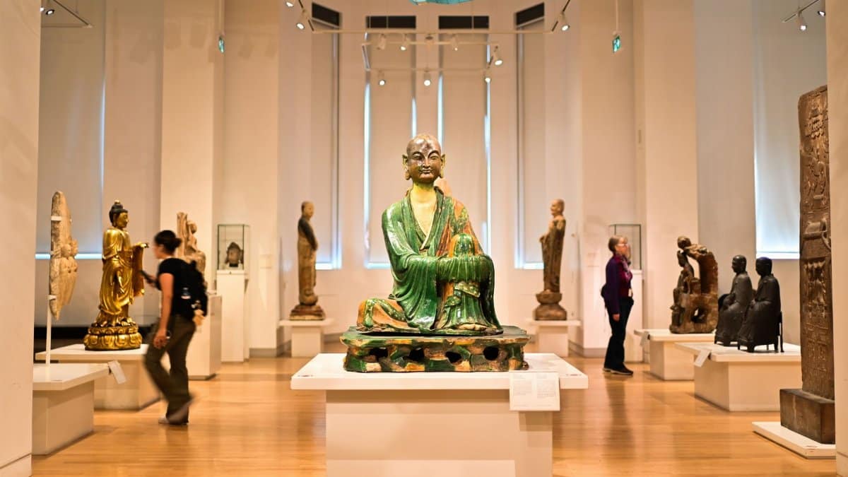 Buddha statues displayed in a museum exhibit with visitors observing.