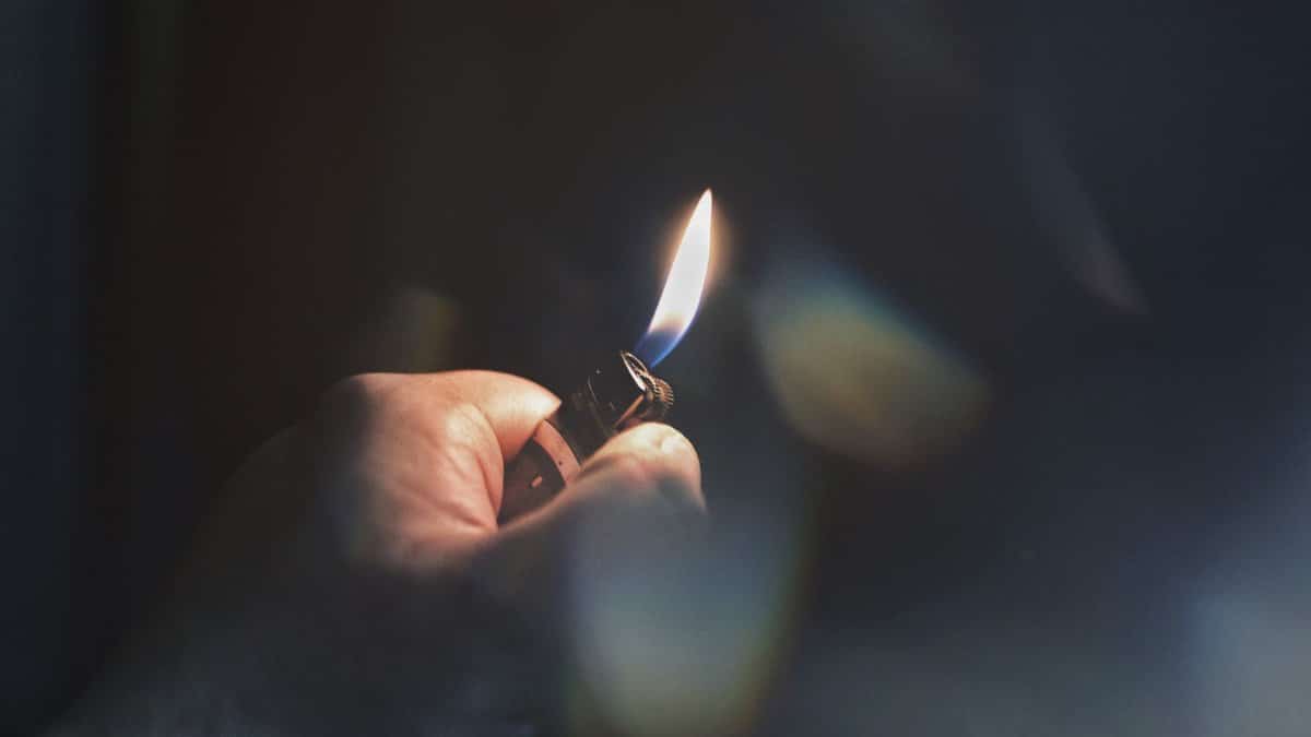 A hand ignites a lighter in a dimly lit environment, focusing on the flame.