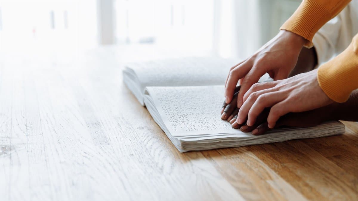 Close-up of hands reading a Braille book, depicting visual impairment education.