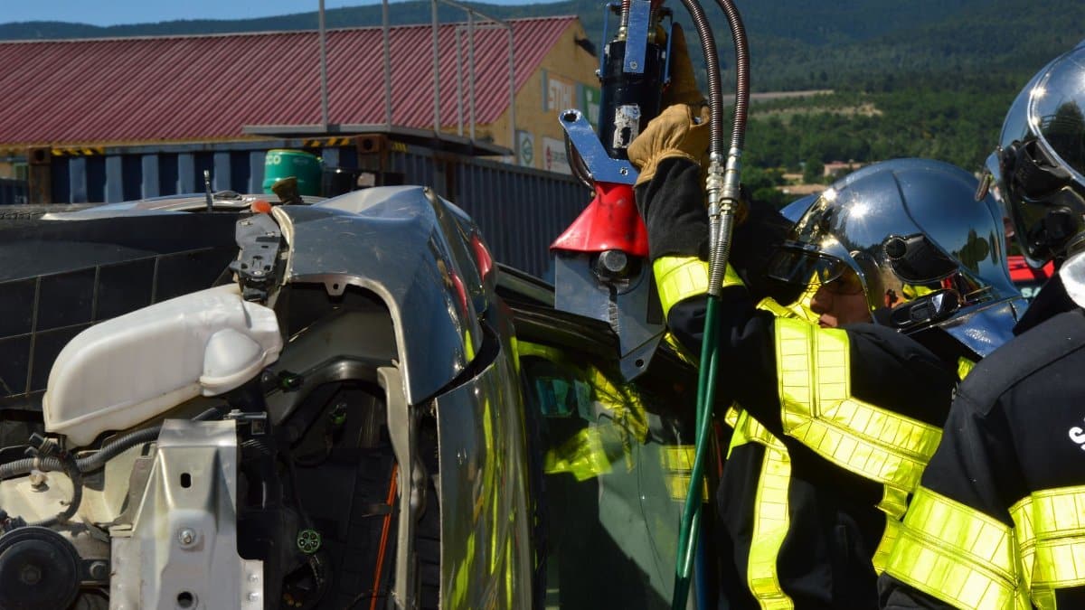 Firefighters in helmets and uniforms conducting an extrication on an overturned vehicle outdoors.