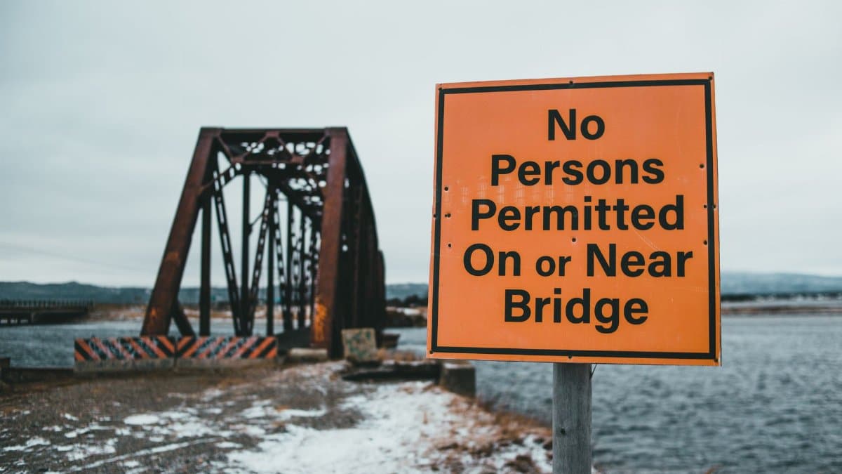 Prohibition sign with title on coast against old bridge above rippled ocean under cloudy sky in winter
