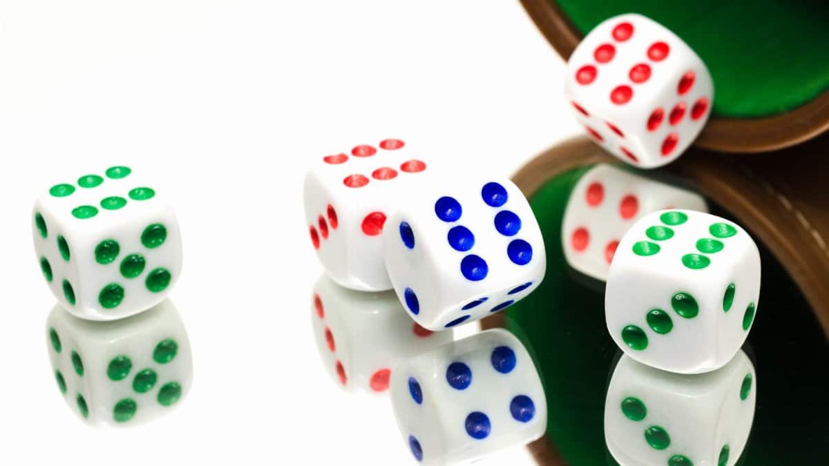 White dice with colorful dots scattered on a reflective surface, evoking gaming and chance.