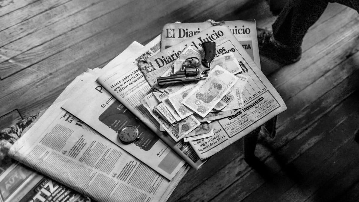 Black and white image featuring currency, newspapers, and a revolver on a wooden surface.