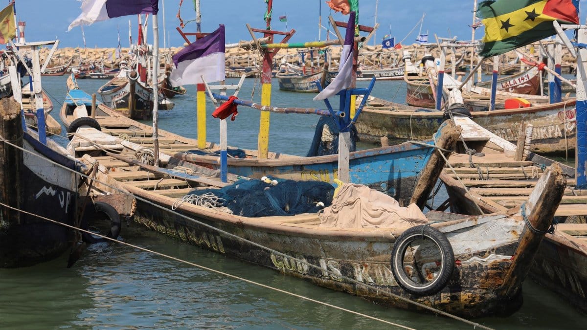 Colorful traditional fishing boats docked at the harbor in Accra, Ghana displaying various flags.