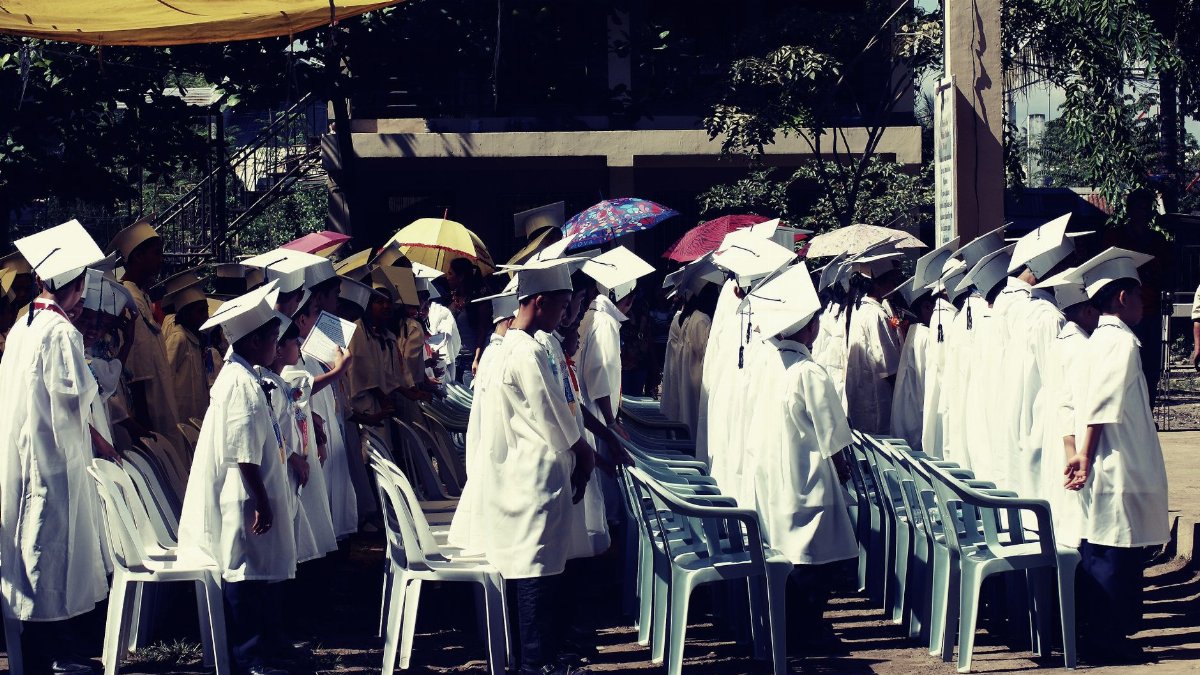 Group of children in academic gowns celebrating graduation outdoors.