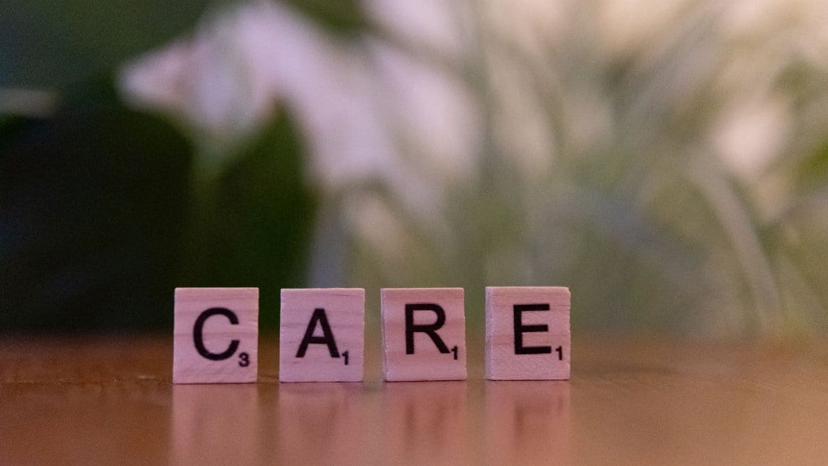 Close-up of wooden tiles spelling 'CARE' on a table with a blurred background, evoking a sense of support.