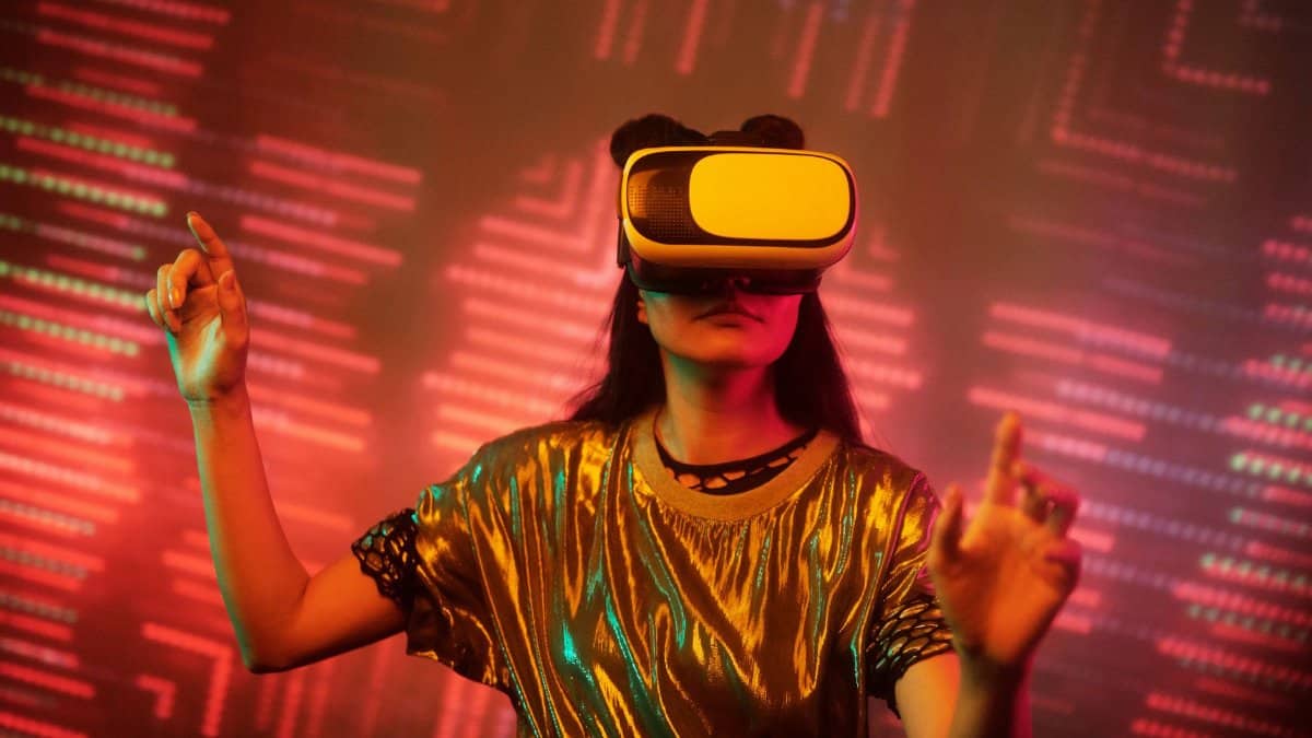 Woman in a metallic top using a virtual reality headset immersed in a digital environment with vibrant lights.