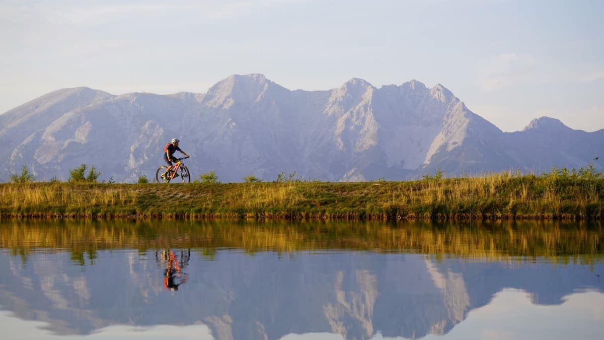 A mountain biker rides along a scenic lake with majestic mountain views in Tirol, Austria.
