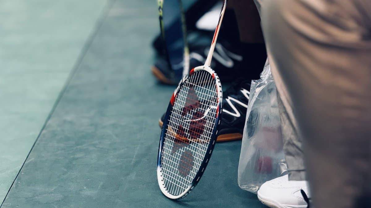 A badminton racket resting on an indoor sports court floor near seated players.