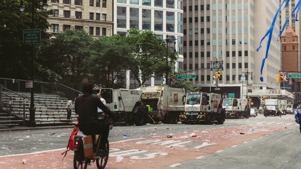 Urban workers clean up debris on a city street following a large parade. Busy environment.