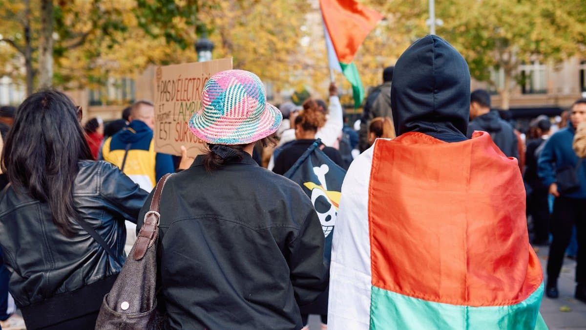 A diverse crowd participates in a peaceful protest in Paris, featuring Malagasy flags and vibrant autumn colors.