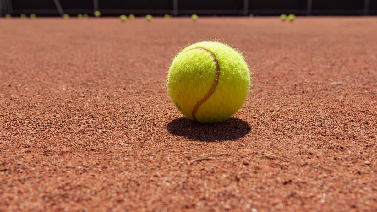 Yellow tennis ball on clay court surface, highlighting texture and sports theme.