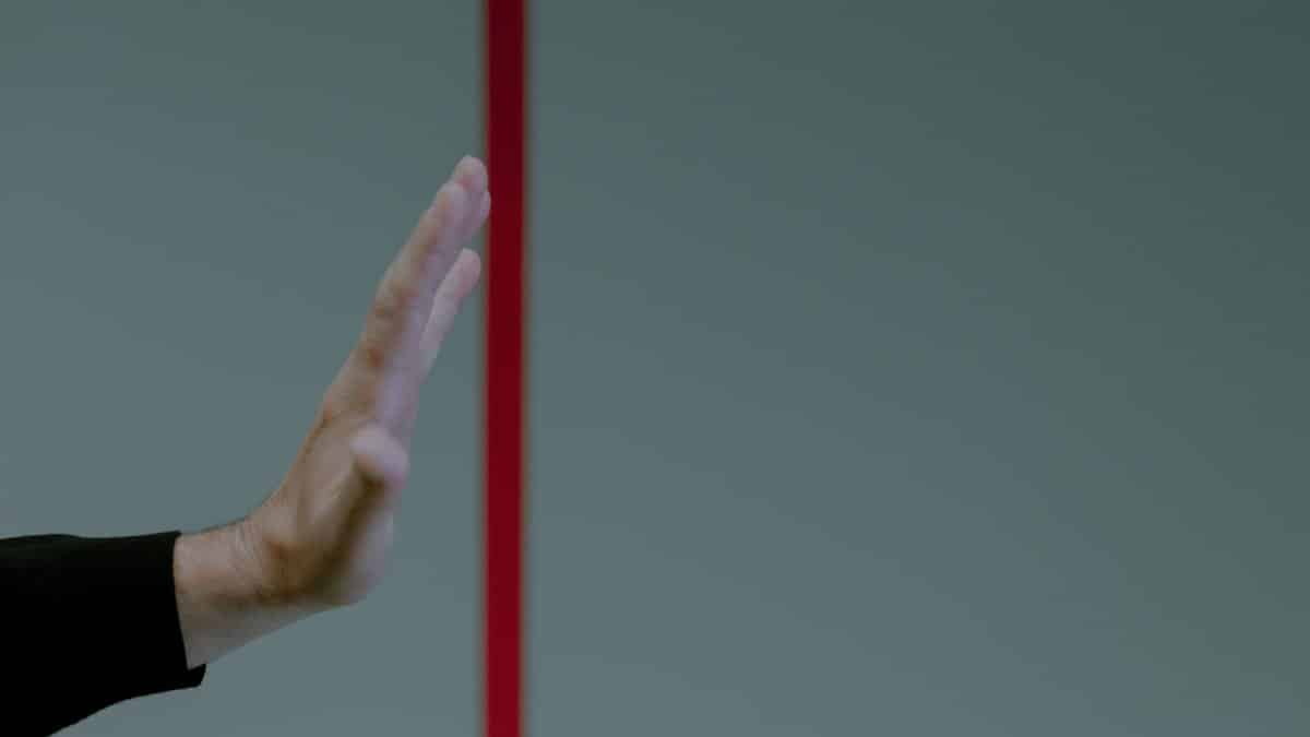 Close-up of a man's hand gesturing stop in front of a vertical red line, concept of boundary.