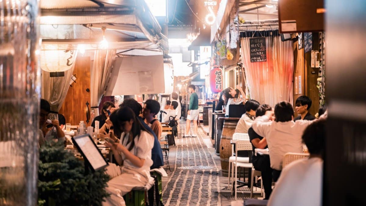 Experience the vibrant nightlife of Osaka's alleyway dining with people enjoying meals and socializing.