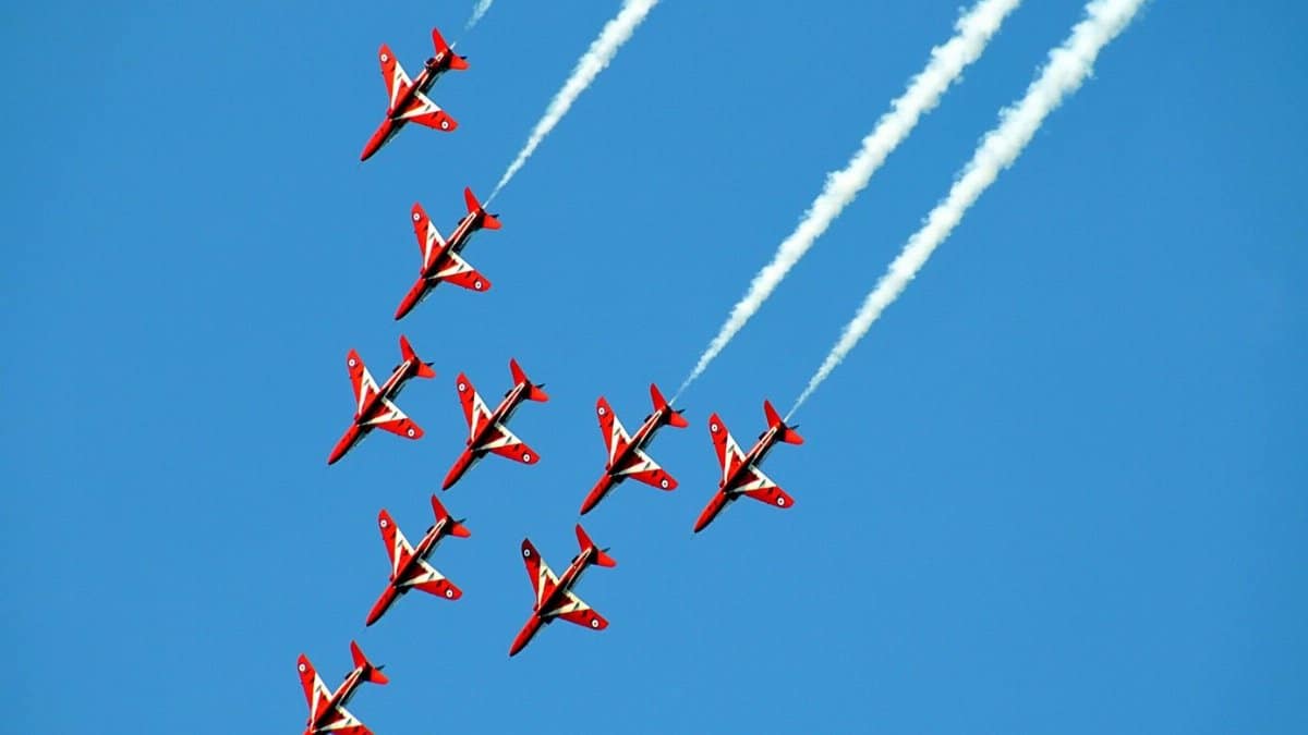 A team of red airplanes performs spectacular aerobatics, leaving trails in a clear blue sky.