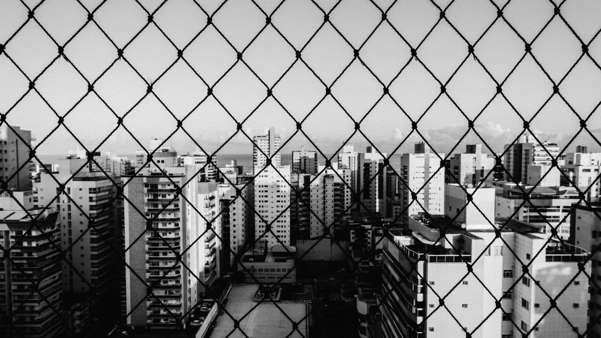 Monochrome view of urban skyscrapers through a chain link fence, highlighting urban architecture.