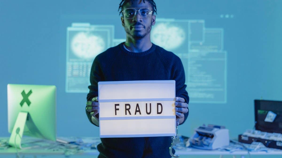 Man holding a 'FRAUD' sign in a tech setting, symbolizing cybersecurity threats.
