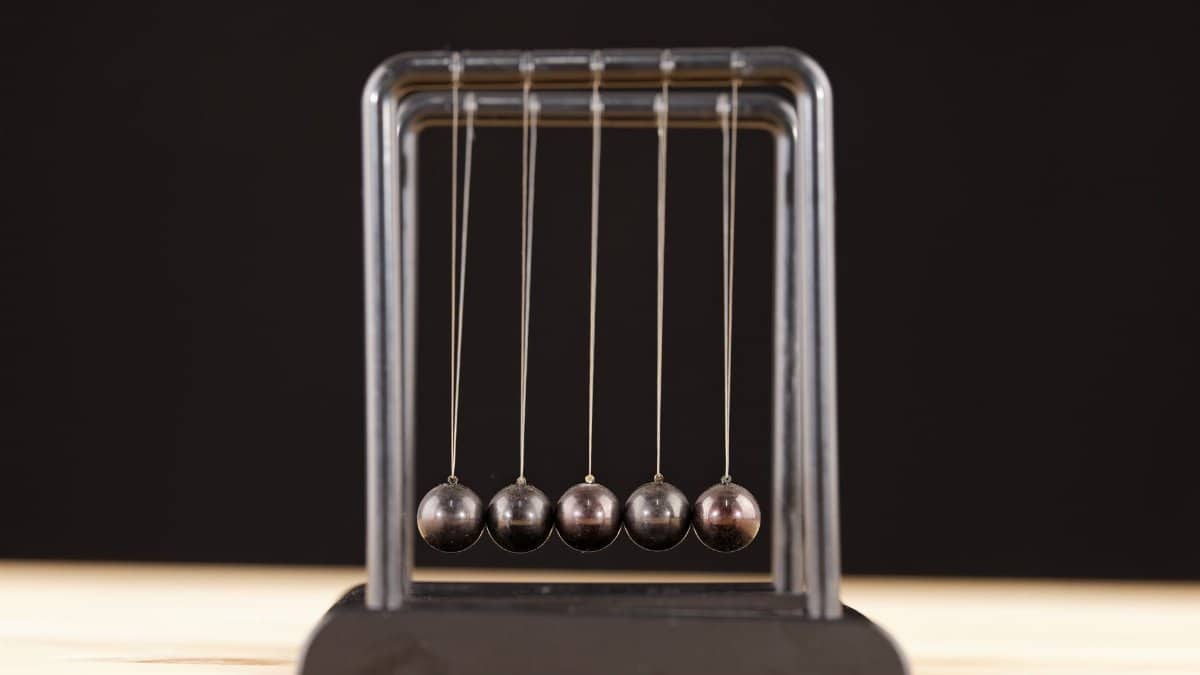 Close-up of a Newton's Cradle resting on a wooden surface against a dark background.