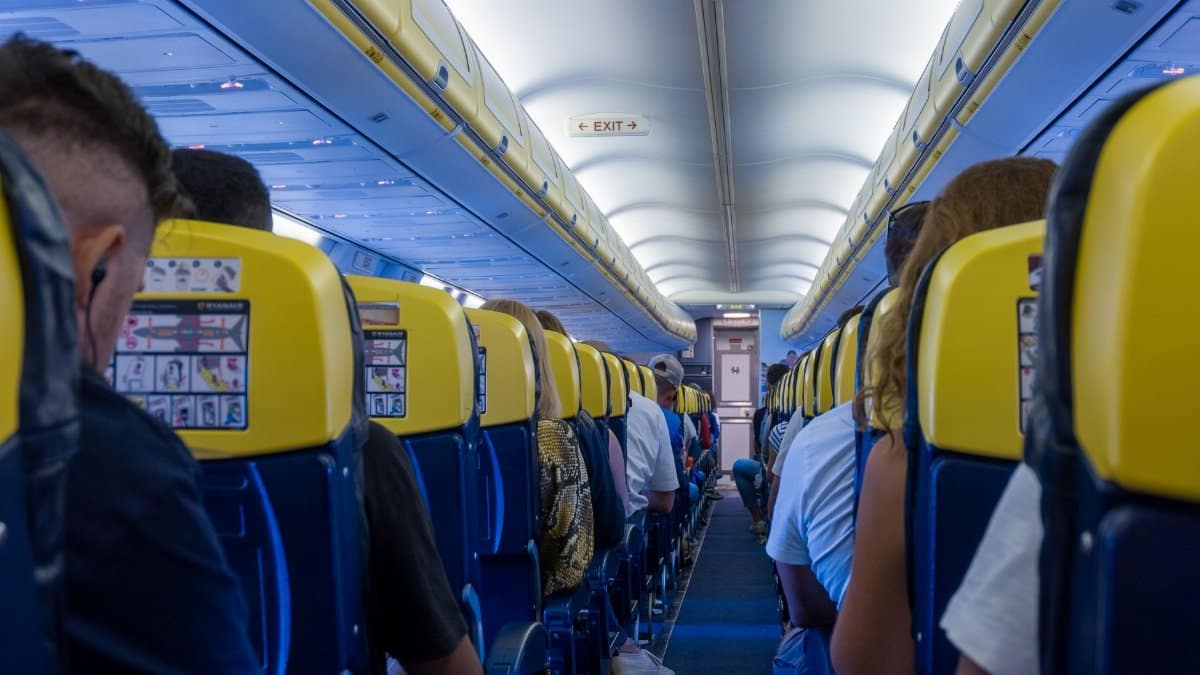 View of passengers seated inside an airplane cabin with yellow seatbacks and overhead bins.