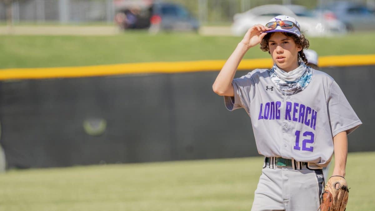 Teen baseball player from Long Reach adjusts his cap during a sunny game outdoors.
