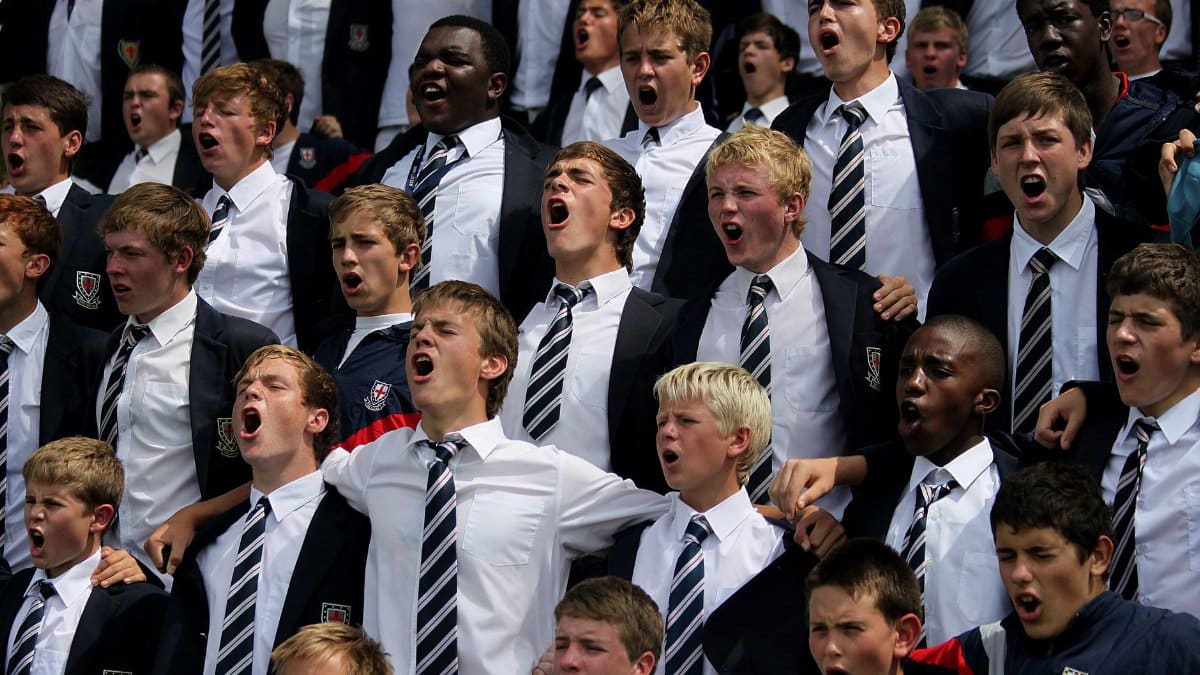 A diverse group of schoolboys in uniforms cheering energetically outdoors.