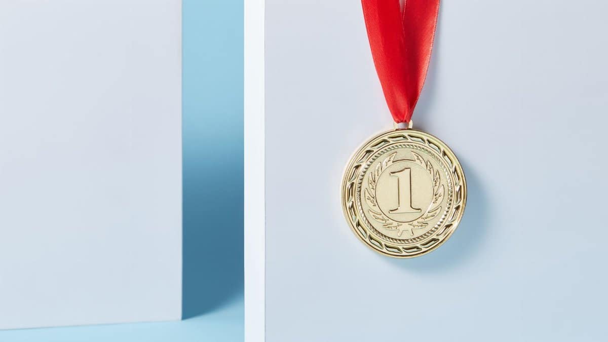 Close-up of a gold medal with a red ribbon hanging against a light blue background.