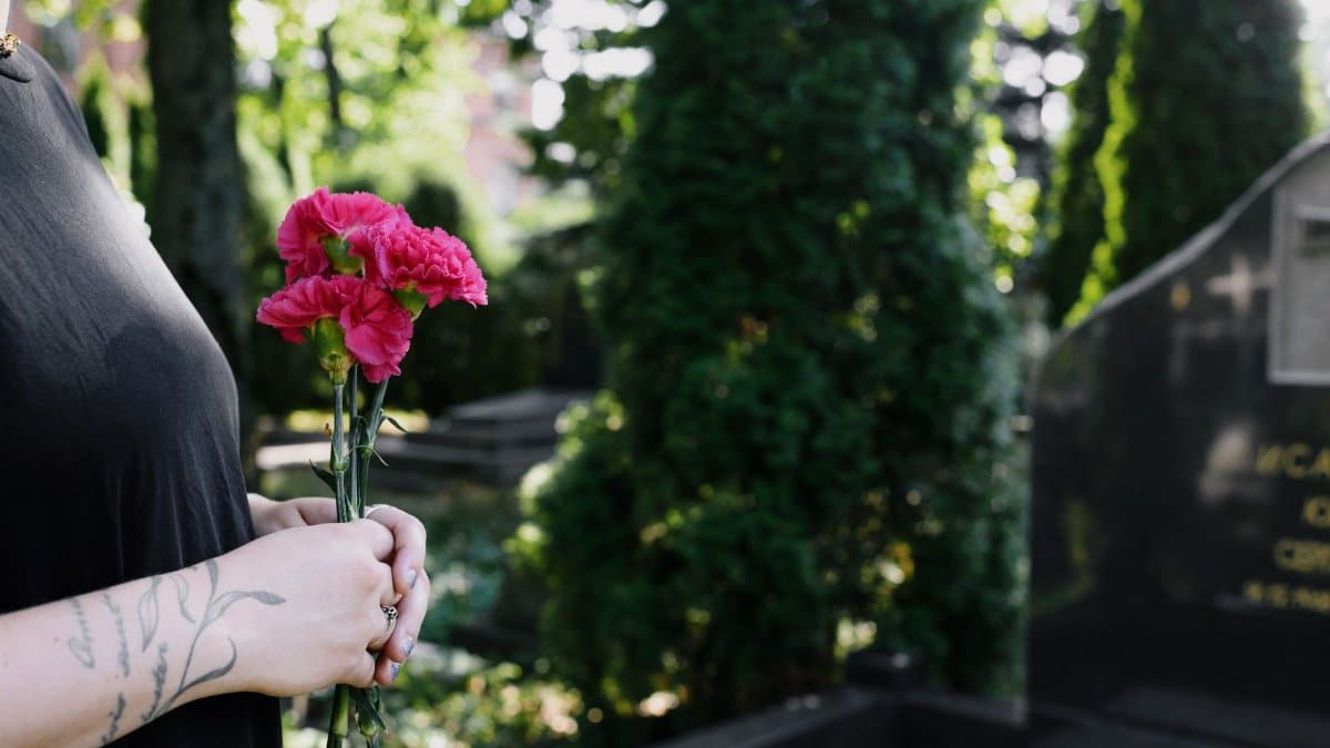A woman holding pink flowers at a cemetery, symbolizing remembrance and affection.