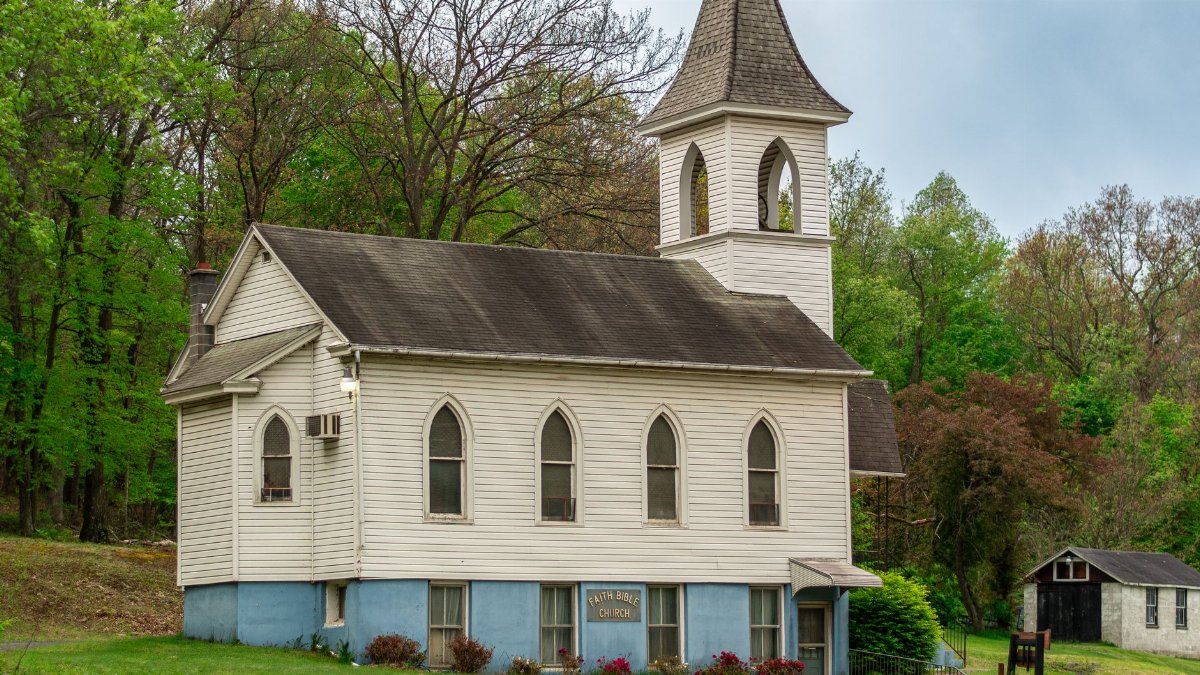 A quaint white church nestled amid lush green trees, evoking serenity in a rural setting.
