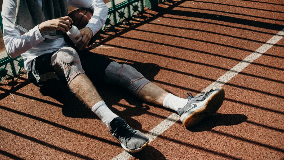 Young male athlete sitting on sports court holding a basketball and water bottle during a break.