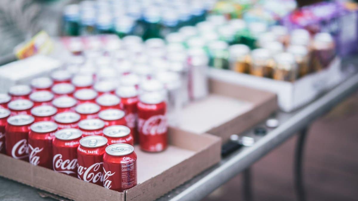 Blurred image of assorted beverage cans on a table, featuring Coca-Cola.
