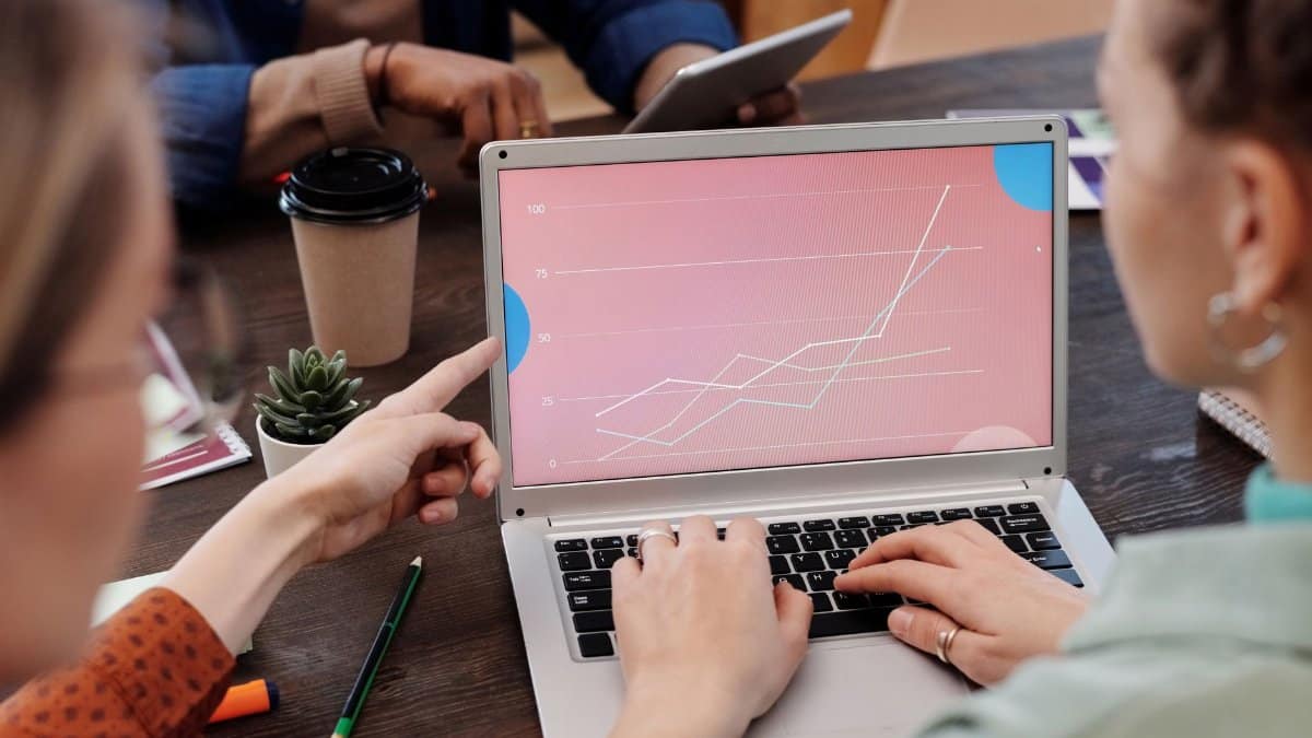 Office workers collaboratively reviewing data trends on a laptop during a meeting.