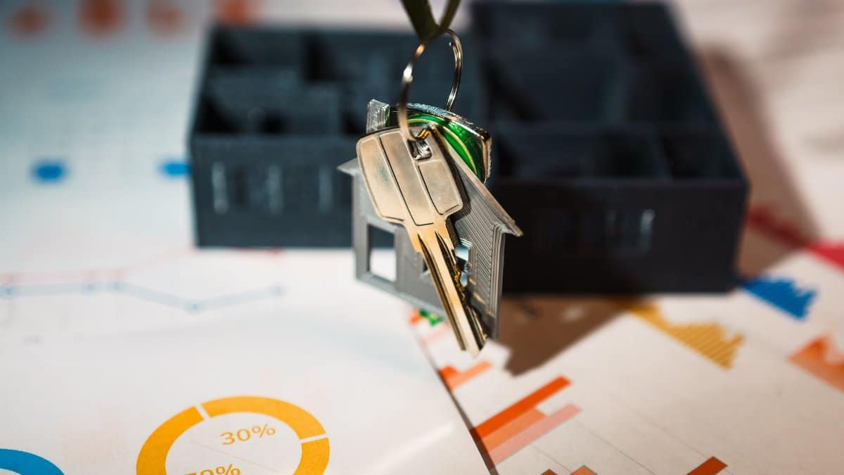 Real estate keys on house keychain with financial graphs, symbolizing property investment.
