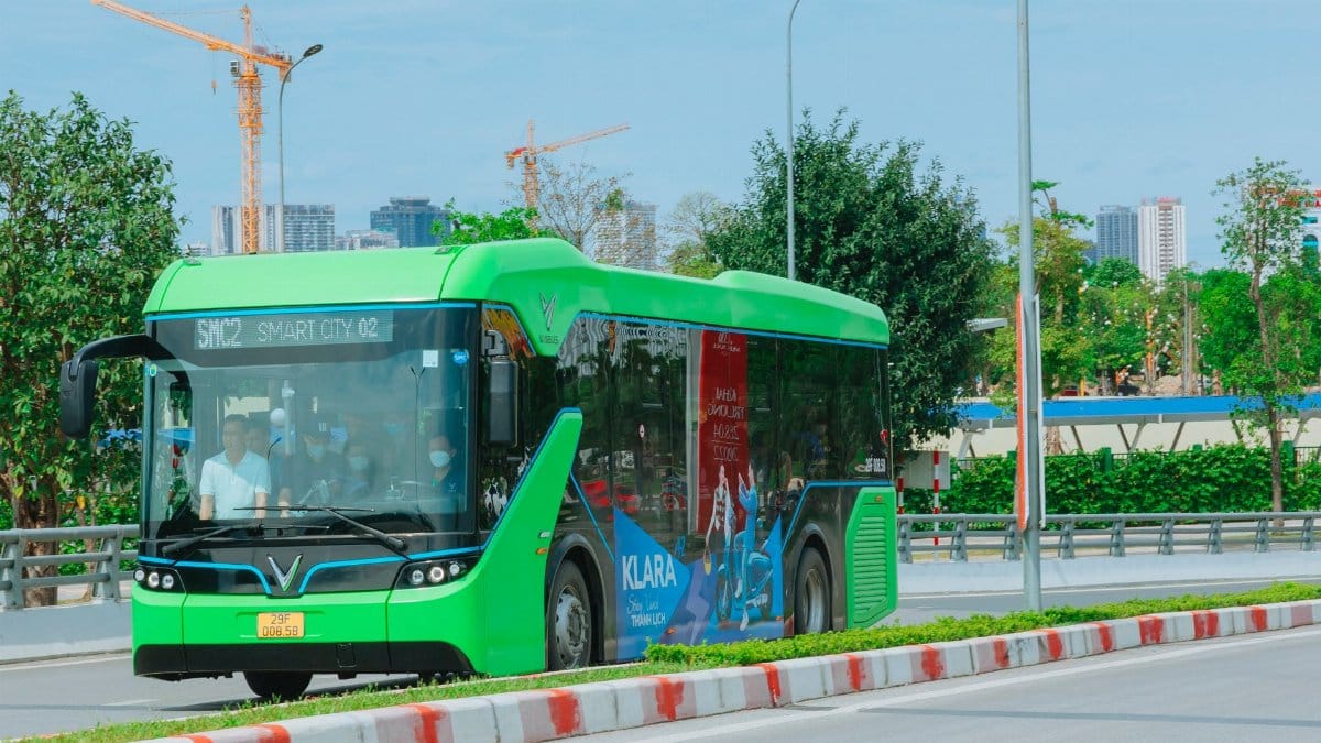 A modern green electric bus travels through Hanoi, showcasing urban transportation and city infrastructure.