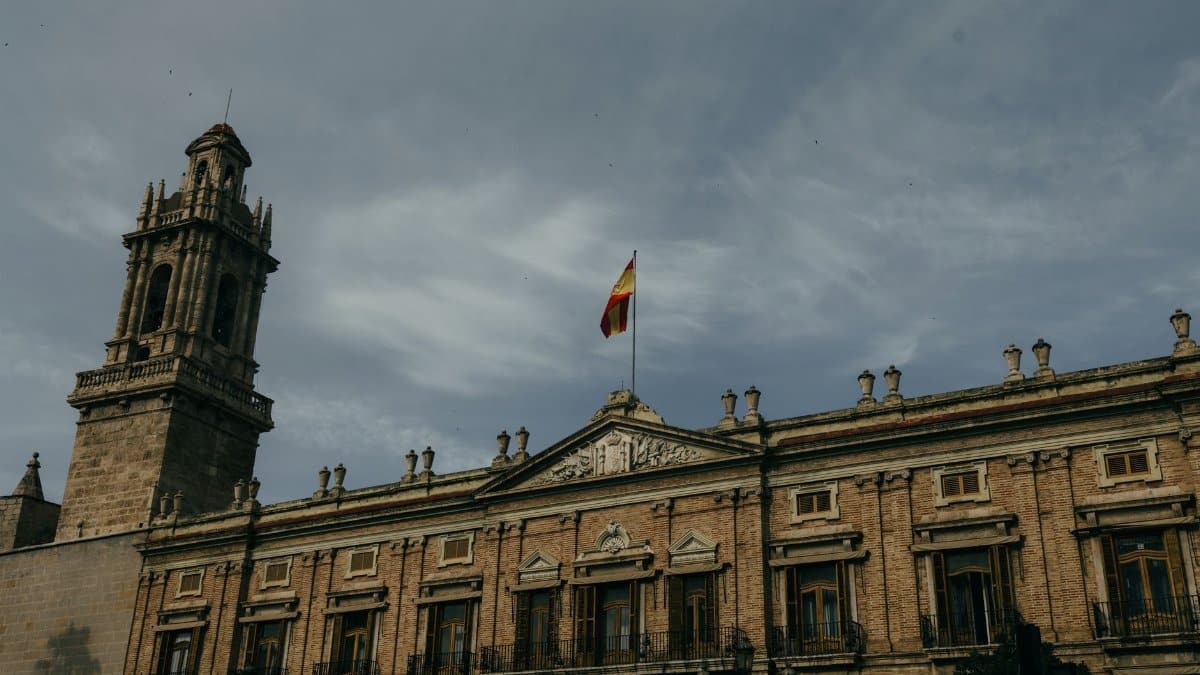 A historic building adorned with a Spanish flag under a cloudy sky in Valencia, Spain.
