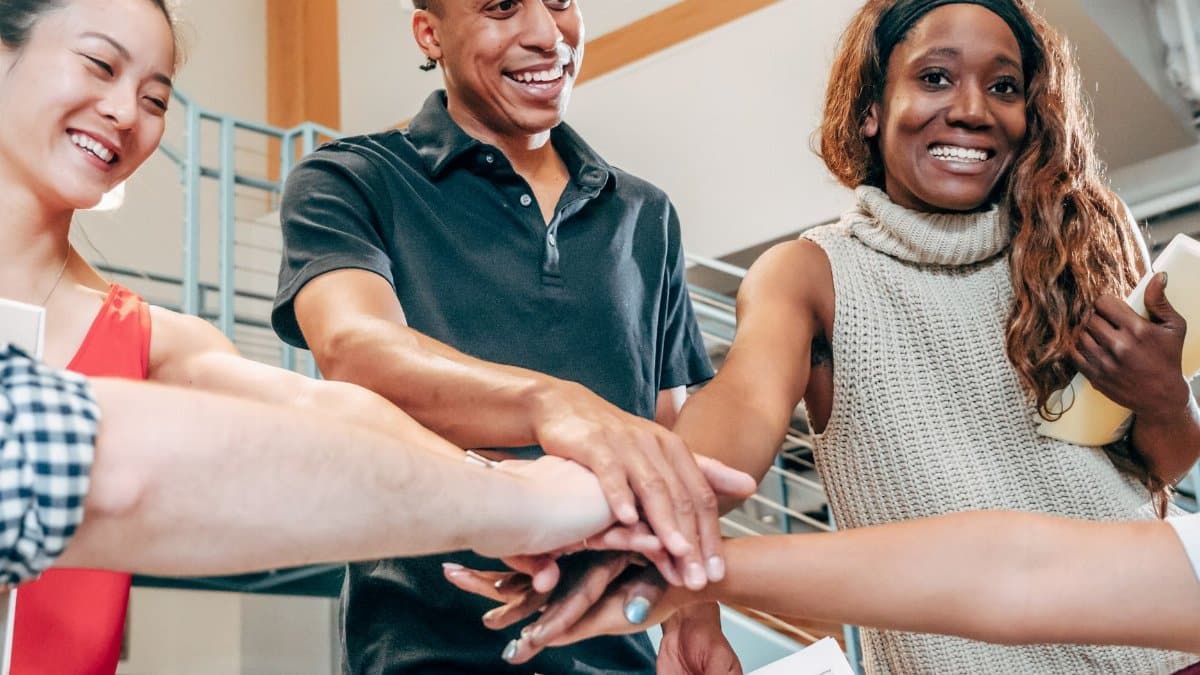 A diverse group of coworkers join hands in an office, showcasing team spirit and collaboration.