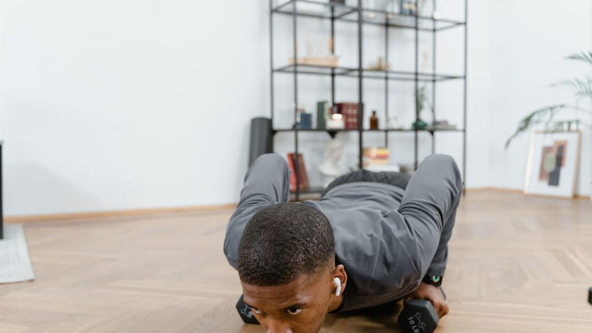 African American man performing push-ups using dumbbells indoors, emphasizing fitness and a healthy lifestyle.
