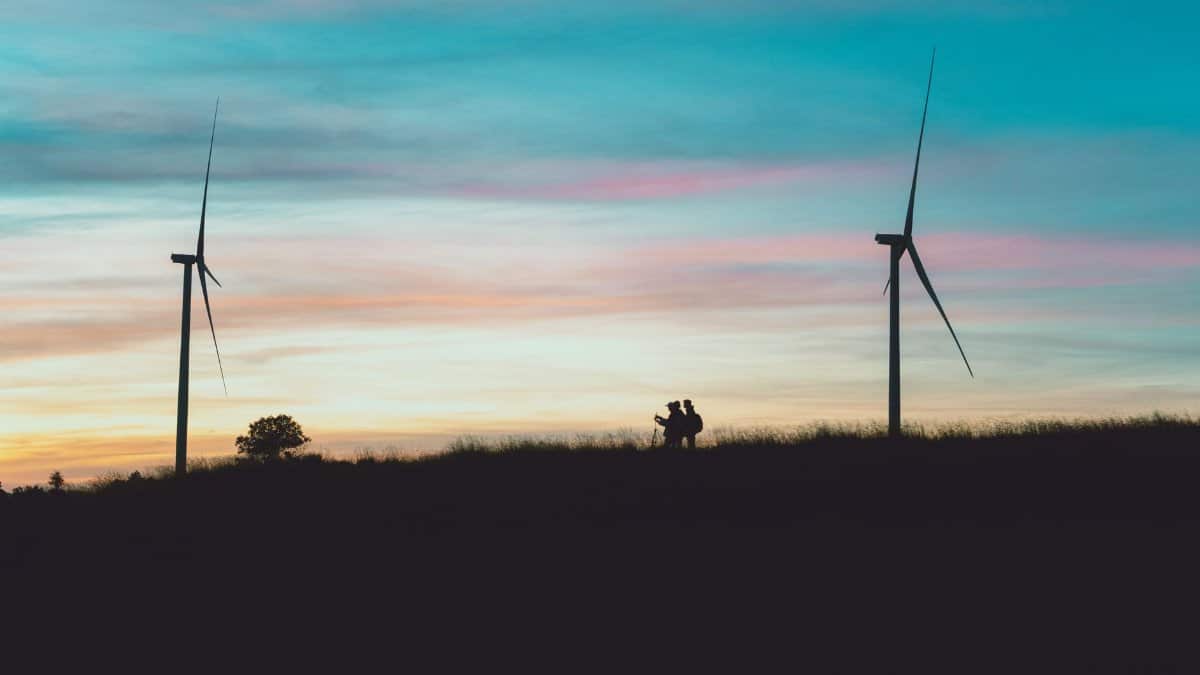 Silhouetted wind turbines and people at sunset in Dalat, Vietnam, capturing renewable energy in scenic highlands.