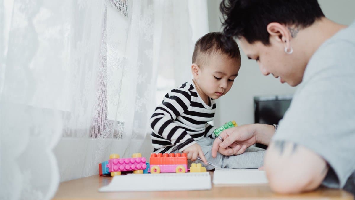 A father and son bonding while playing with colorful building blocks on a table indoors.