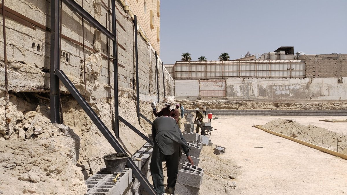 Workers building a concrete block retaining wall at a construction site under the clear sky.