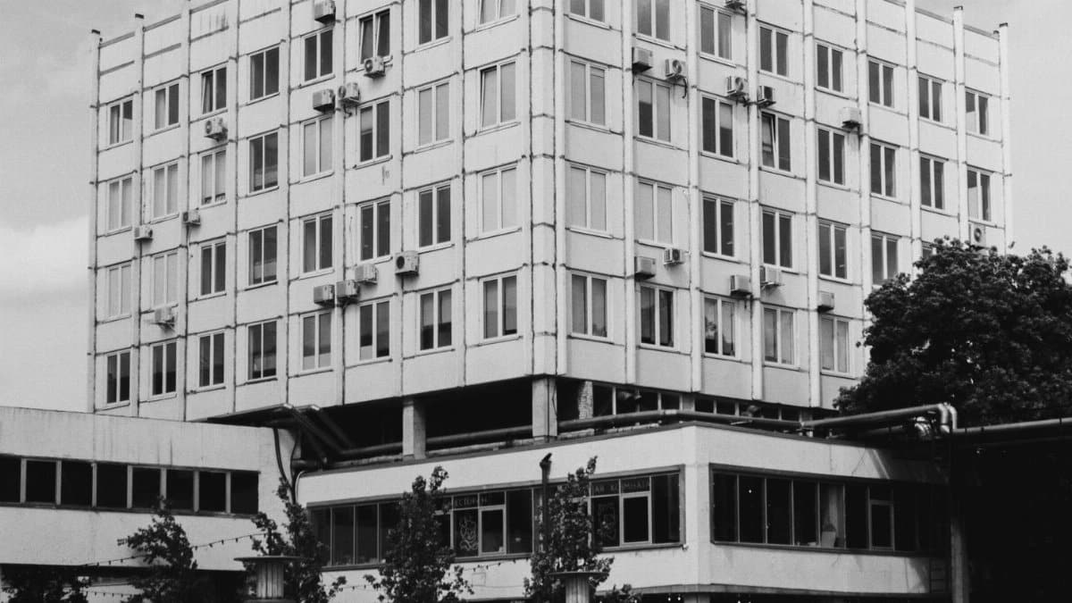 Black and white photo of a modernist building with people walking nearby, highlighting urban architecture.