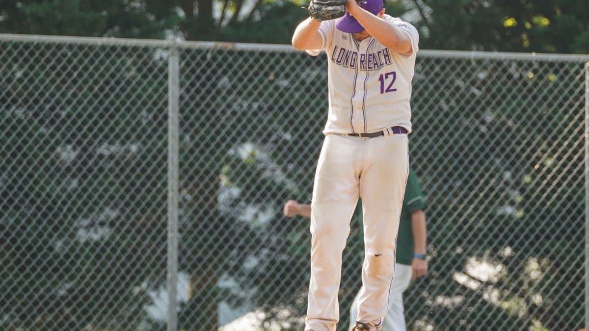 A baseball player in a Long Reach uniform prepares to pitch on a sunny day.