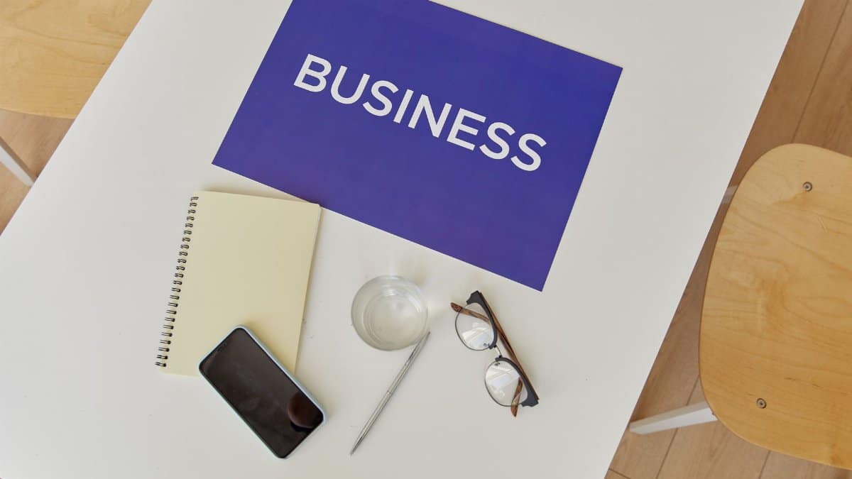 Top view of a minimalist business workspace with essentials like notebook, phone, glasses, and a business sign.