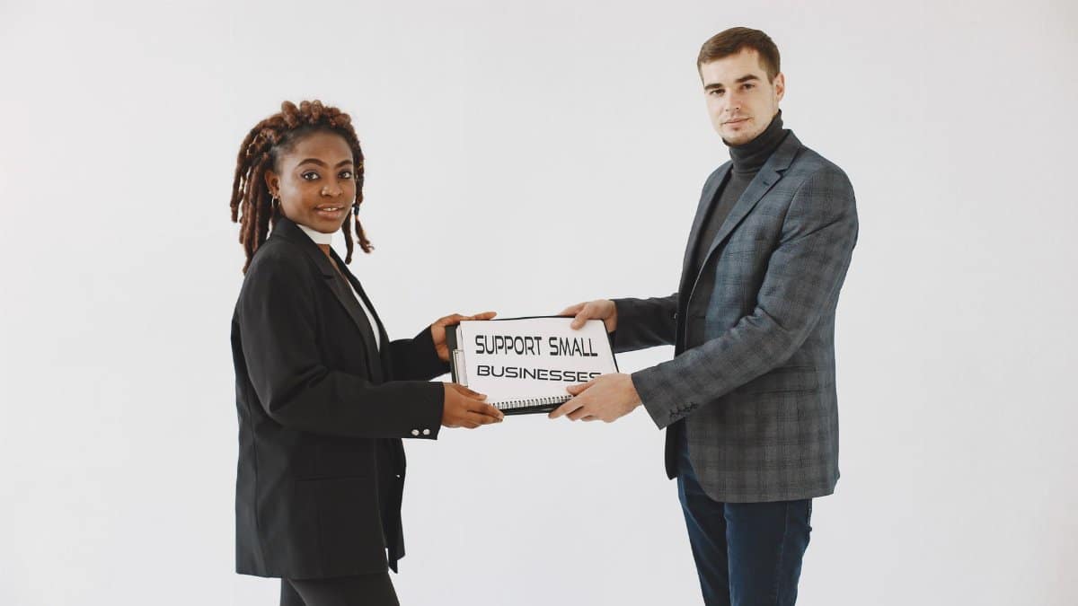 Two diverse business professionals promoting small business support with a sign.