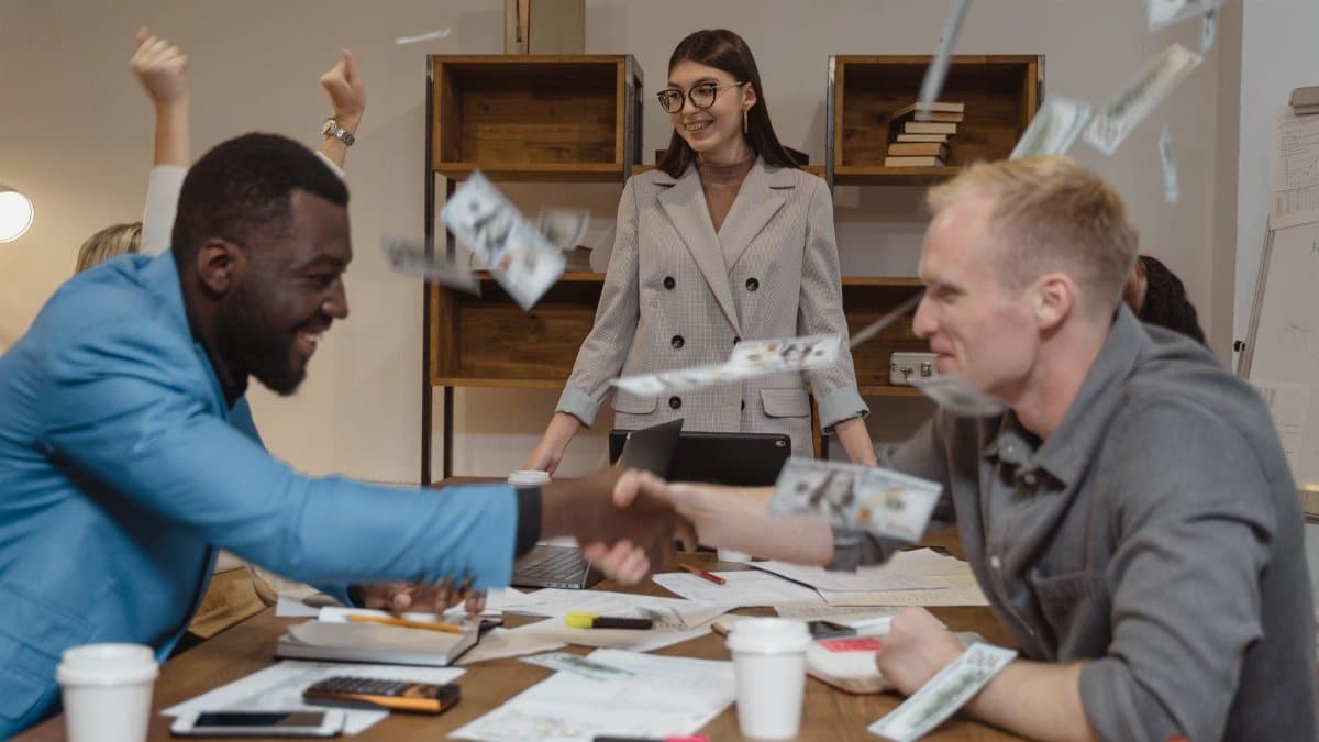 Joyful business colleagues celebrating a successful deal with handshake and flying money.