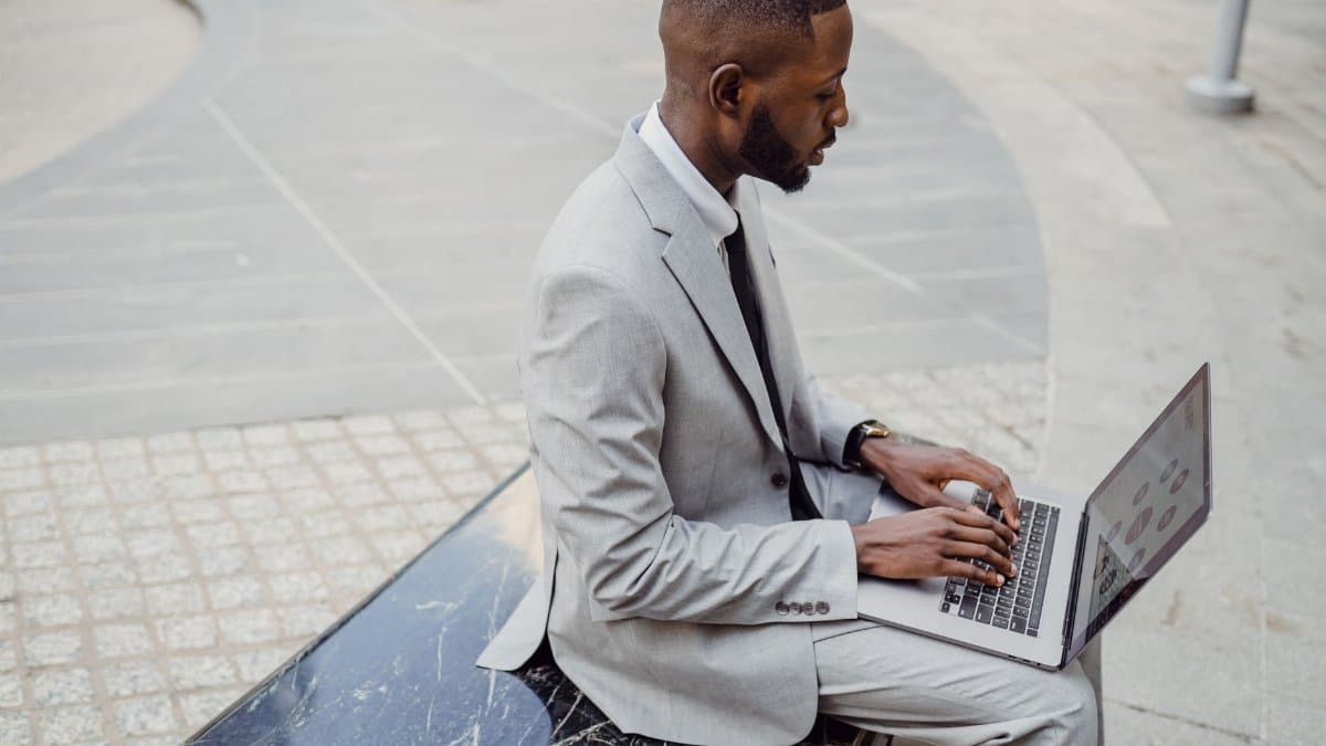 Business professional in a suit working on a laptop outdoors in an urban location.
