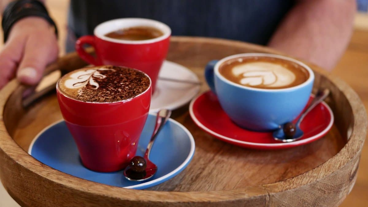 Three colorful cups of coffee with latte art on a round wooden tray, perfect for coffee lovers.