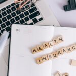 Scrabble tiles spelling health insurance on a planner next to a laptop.