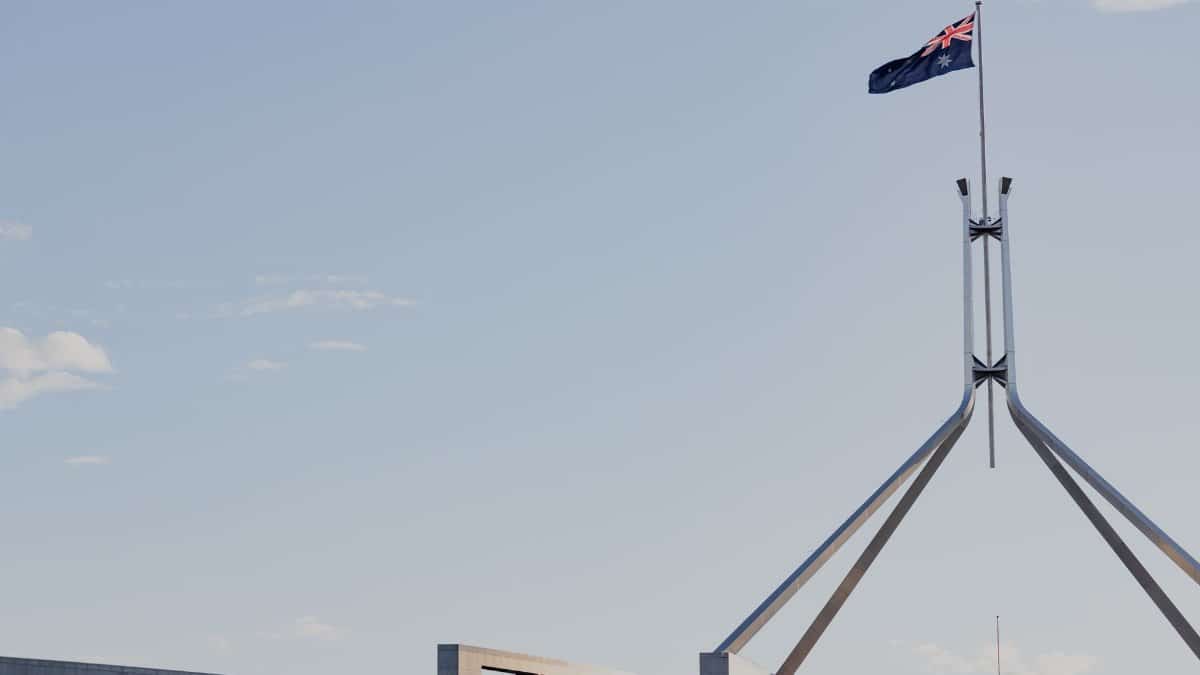 Canberra's iconic Australian Parliament House with national flag against a clear blue sky.